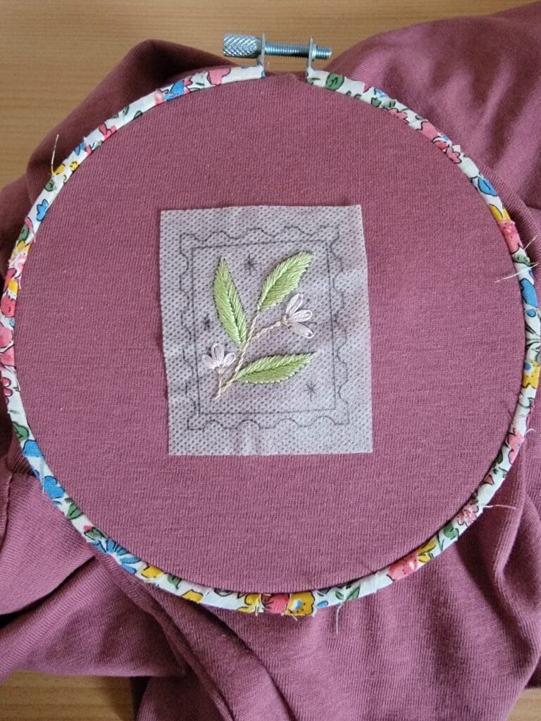 motif-a-broder-fleurs motif à broder soluble en cours de broderie sur un tee shirt et qui représente un timbre floral