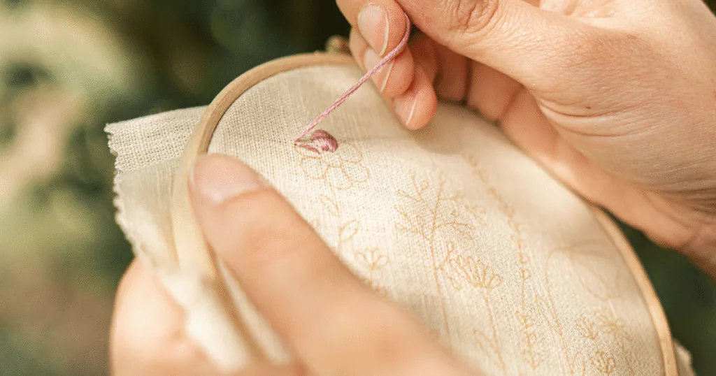 Mains en train d'apprendre la broderie en pleine nature, moment de pause et de créativité.