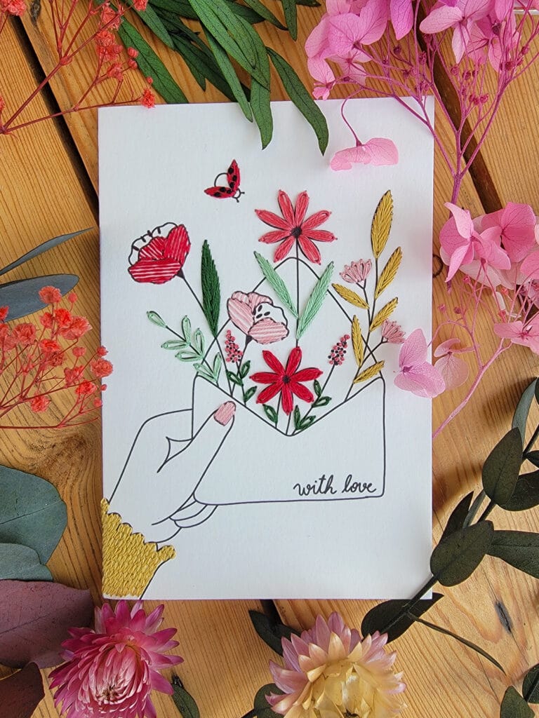 Carte à broder représentant une main tenant une enveloppe à offrir avec des fleurs !