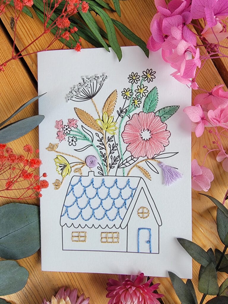 Carte à broder représentant une maison de campagne dont le toit se fleurit