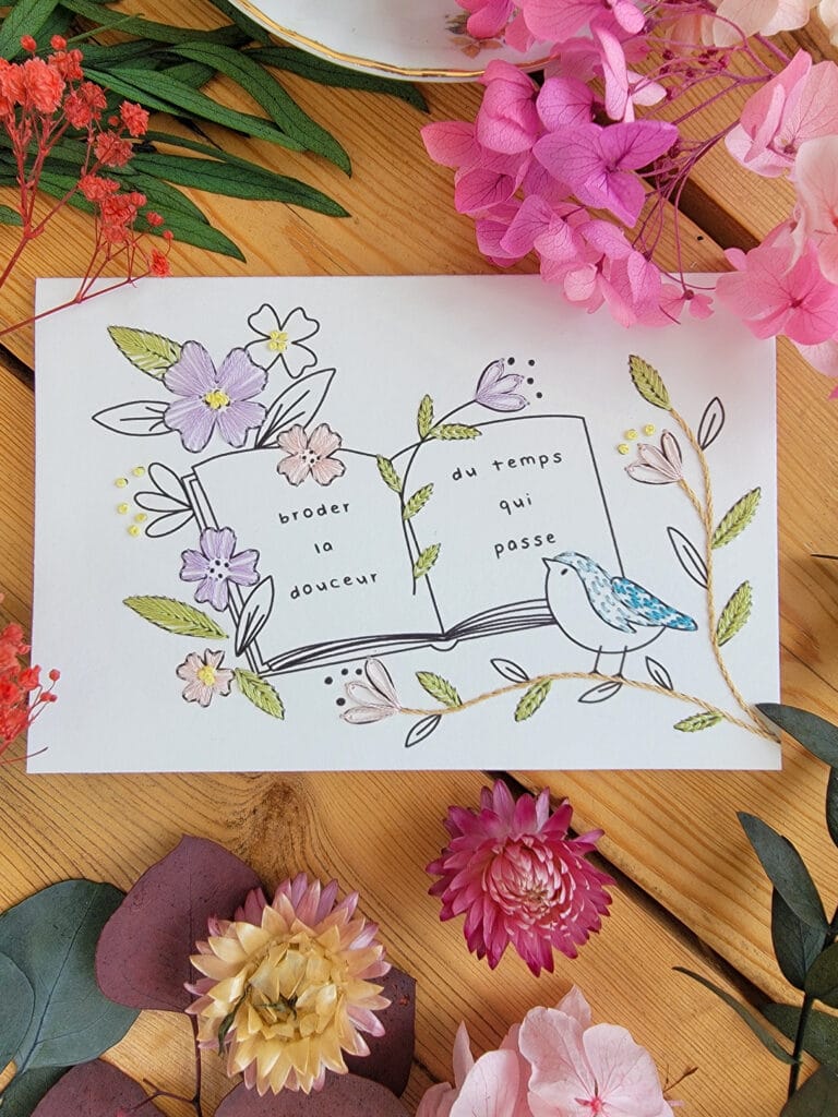 Carte à broder représentant un livre ouvert où est inscrit "Broder la douceur du temps qui passe" et illustrant un oiseau.